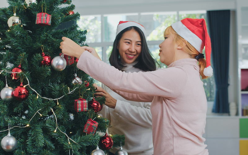 Two people fixing a tree with Christmas lights.